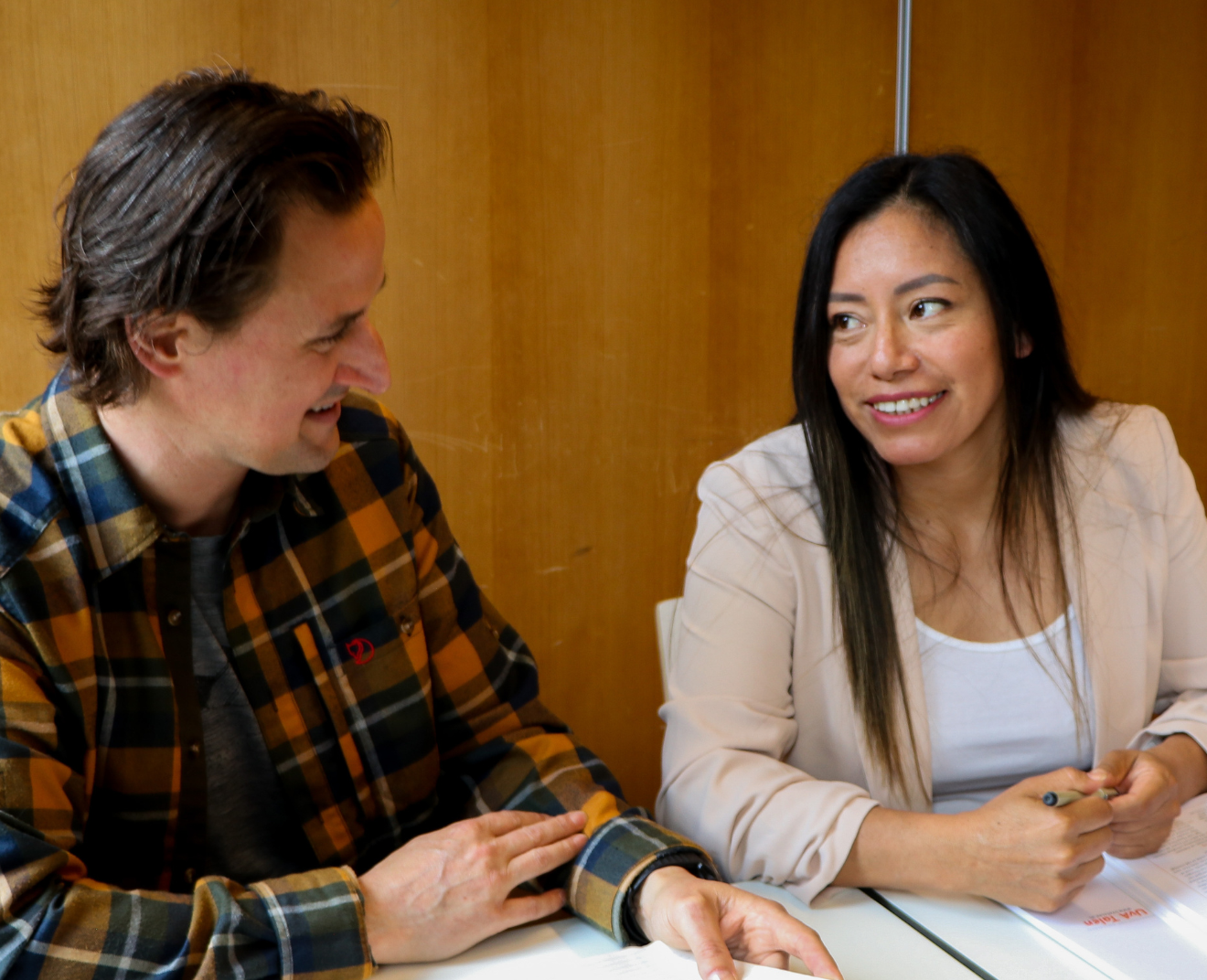 Een man en een vrouw zitten samen aan een tafel en voeren een gesprek terwijl ze lachen. Ze hebben studieboeken en notities voor zich liggen.