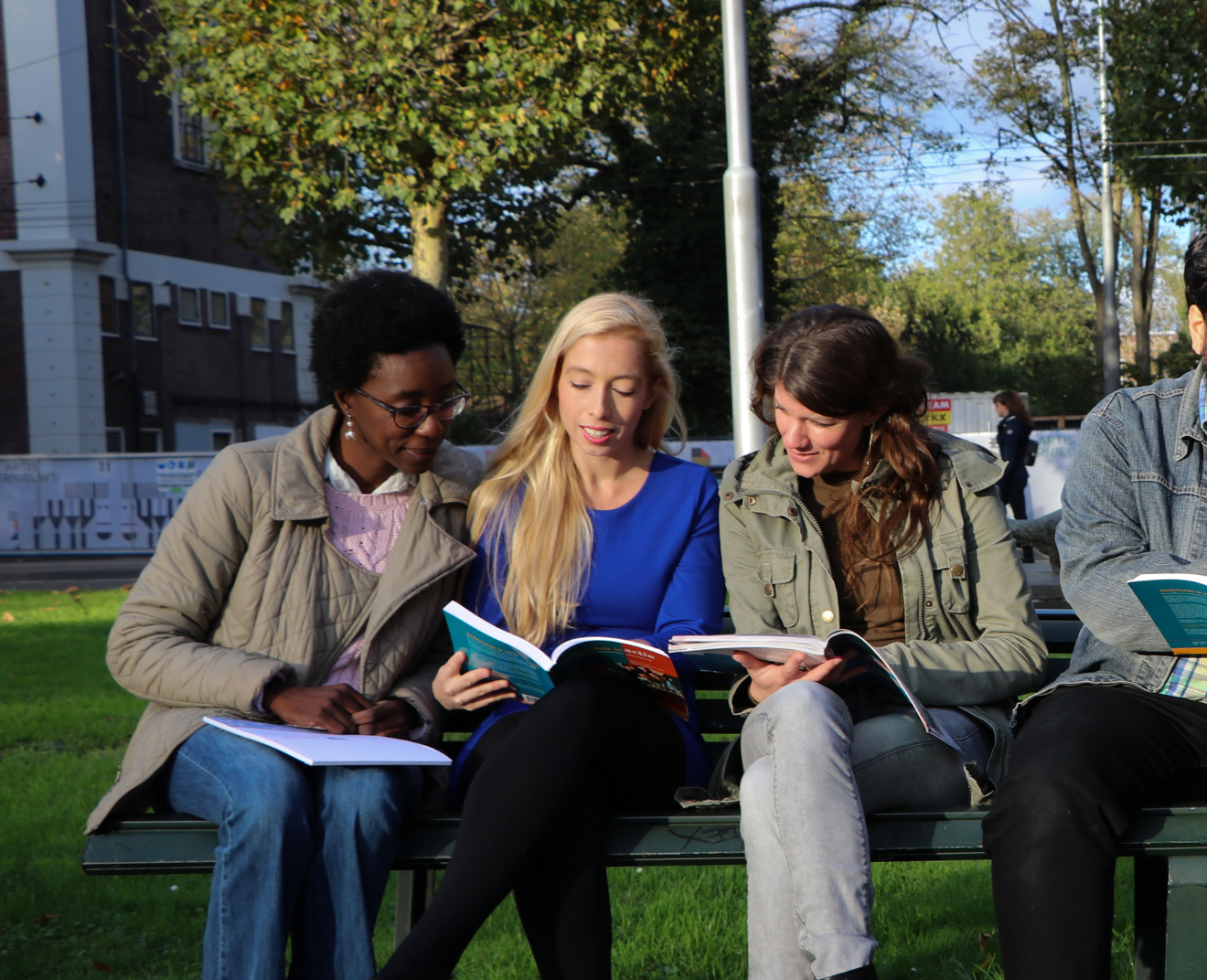 Drie vrouwen zitten samen op een bankje in het park en kijken in studieboeken. Ze lijken in gesprek en delen informatie.
