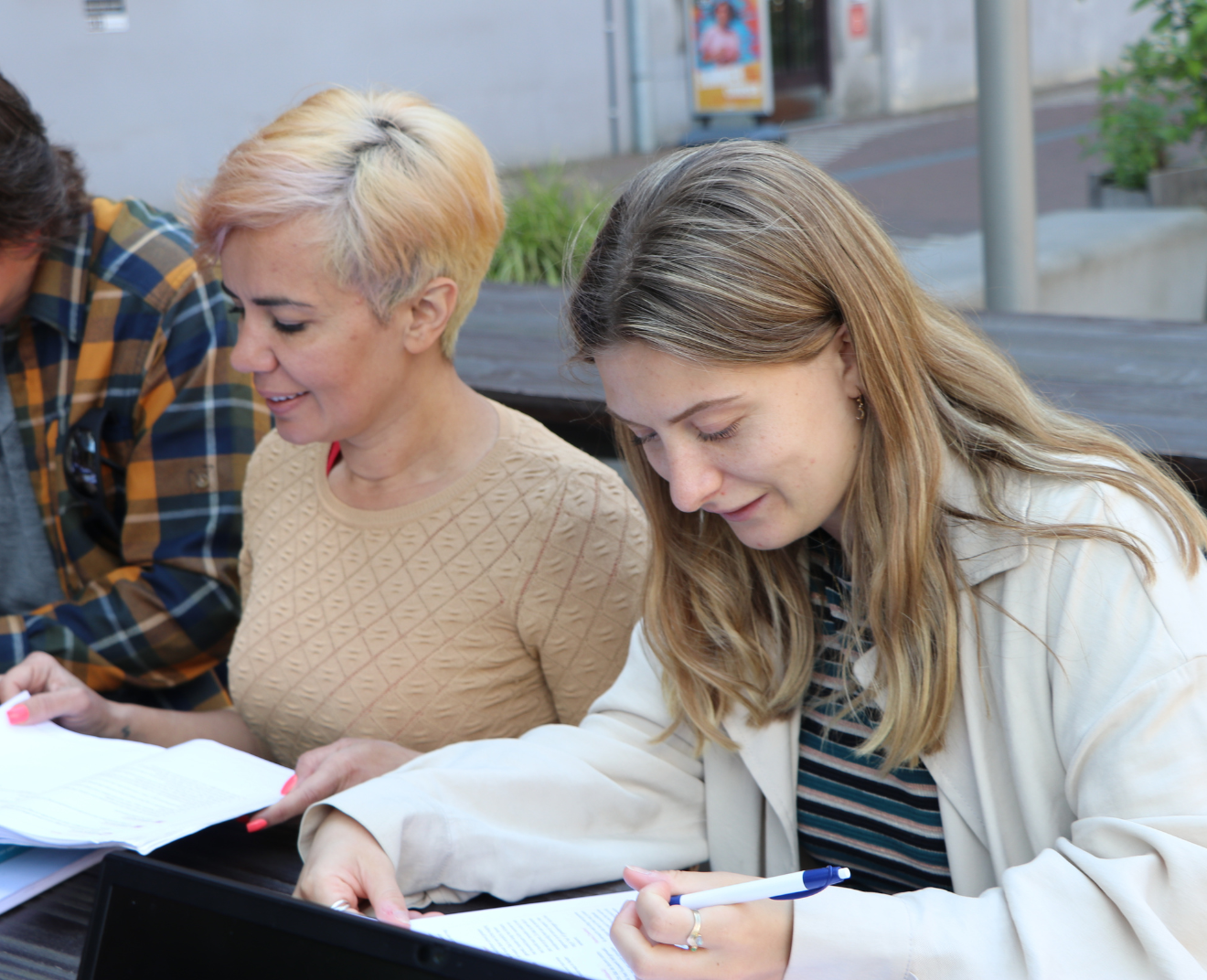 Twee vrouwen werken buiten aan een tafel, één lachend en de ander schrijvend.