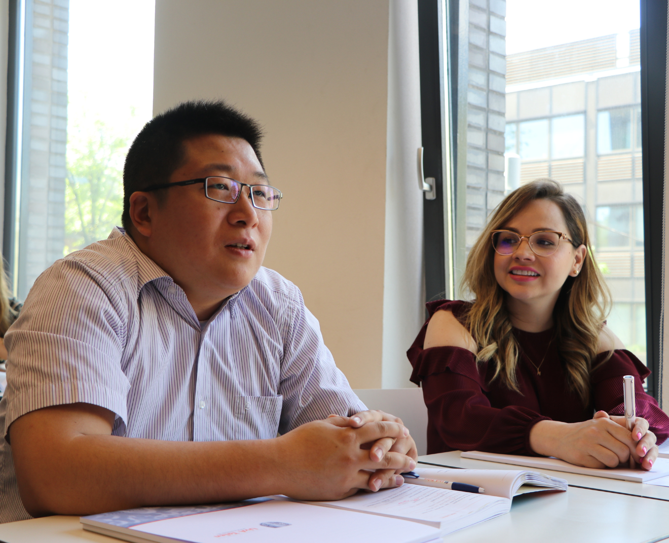Twee studenten zijn in gesprek tijdens een les, waarbij de een spreekt en de ander aandachtig luistert.