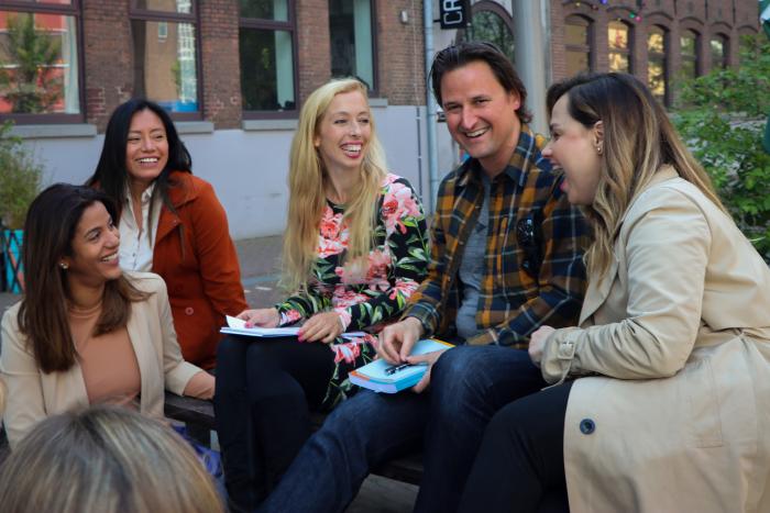 Five people sitting on bench in Amsterdam studying from a Dutch Beginners course book before their lesson at UvA Talen