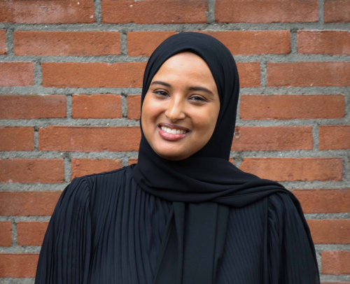 Een portretfoto van medewerker van UvA Talen Yasmien voor een stenen muur